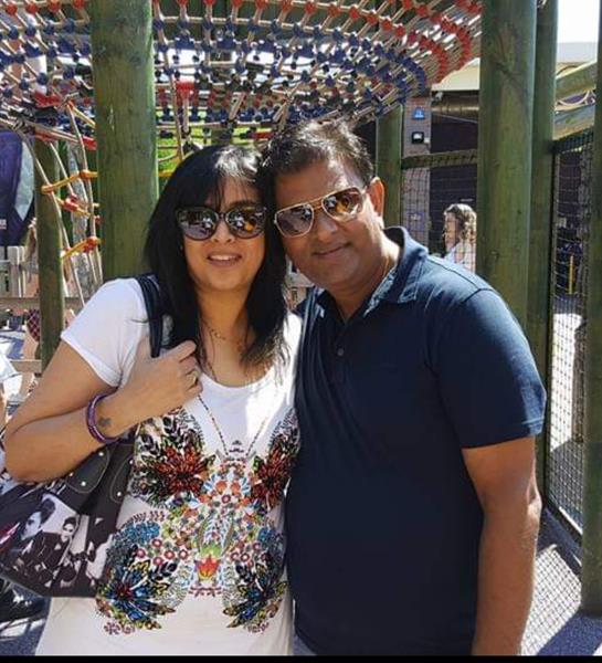 A couple smiles while posing together in a busy outdoor playground under bright sunshine.