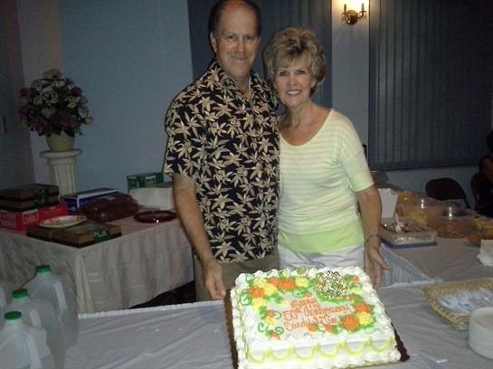 A couple enjoys a joyful celebration at a gathering with a vibrant cake and elegant decor.