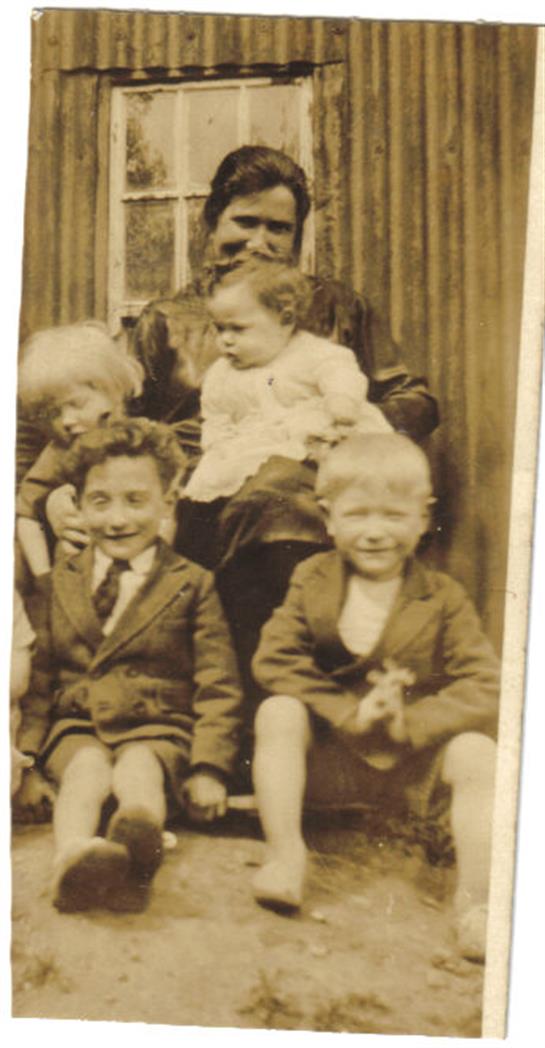 Children happily pose with a woman on the steps of a worn building, capturing nostalgia.