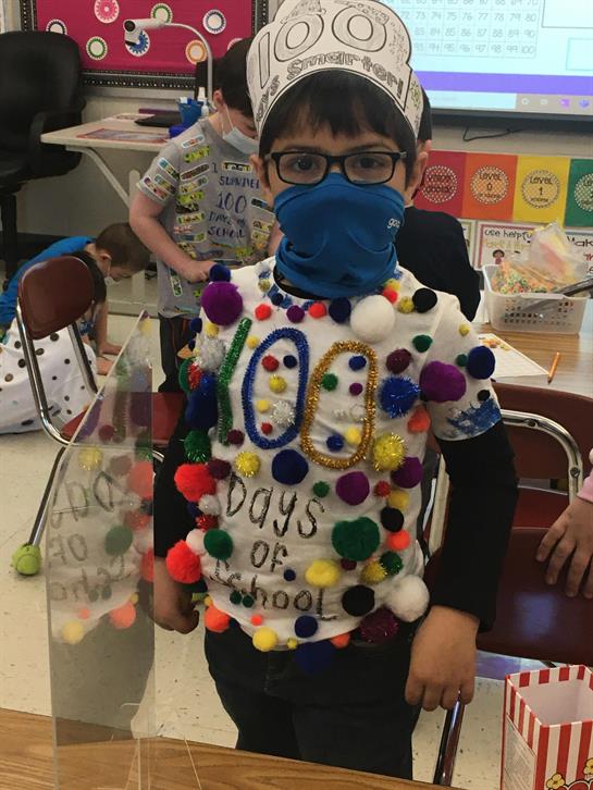 A student proudly showcases a costume adorned with pom-poms for 100 days of school celebration.