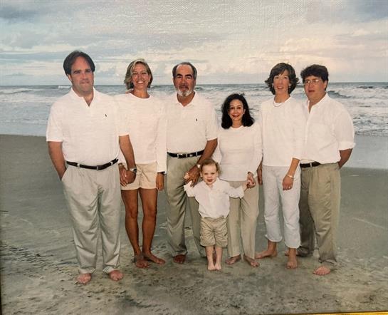 Seven family members celebrate together at the beach, wearing white outfits and enjoying the moment.