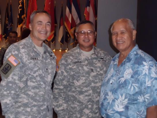 Three men stand together smiling at a gathering adorned with various international flags.