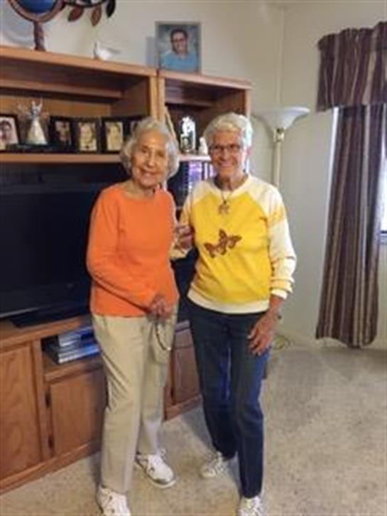 Two friends smile together in a cozy living room filled with family photos.