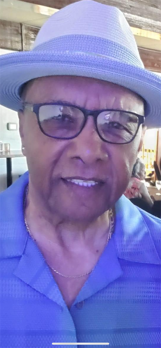An elderly man is smiling while wearing glasses and a light blue hat inside a busy restaurant.