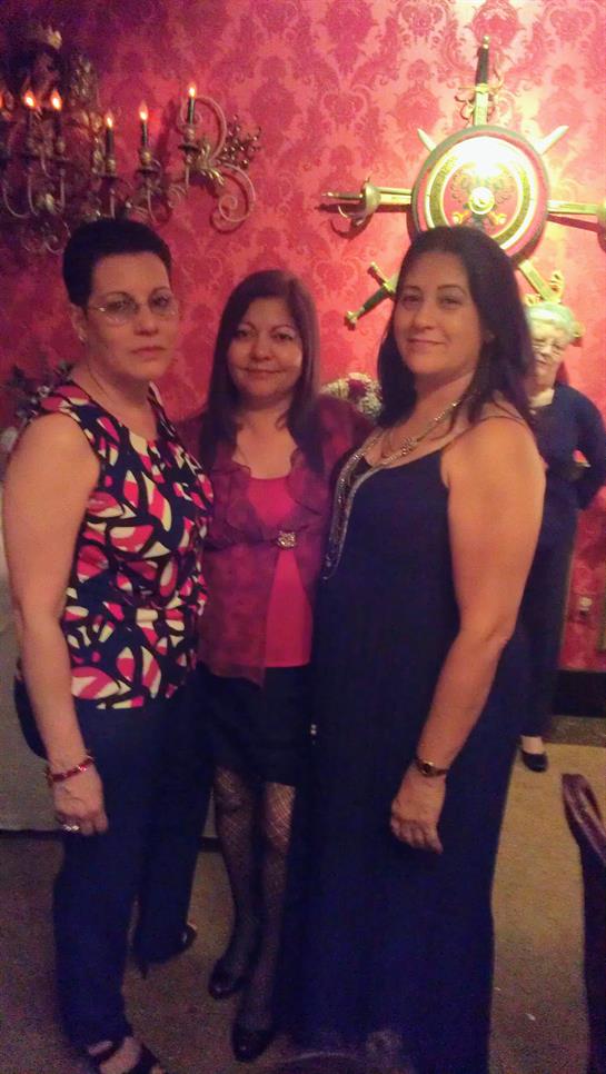 Three women stand together, smiling at the camera, in a lively venue adorned with decor.