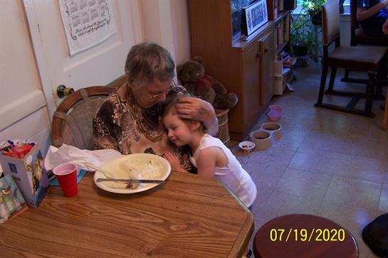 A child hugs her grandmother while they enjoy a meal at the kitchen table.