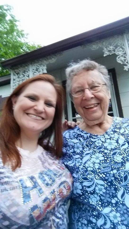 A young woman and her grandmother stand together smiling, enjoying a warm day outdoors.