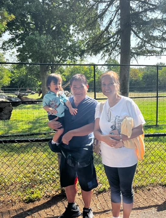 A family poses together at a park, smiling and enjoying a sunny day outdoors.