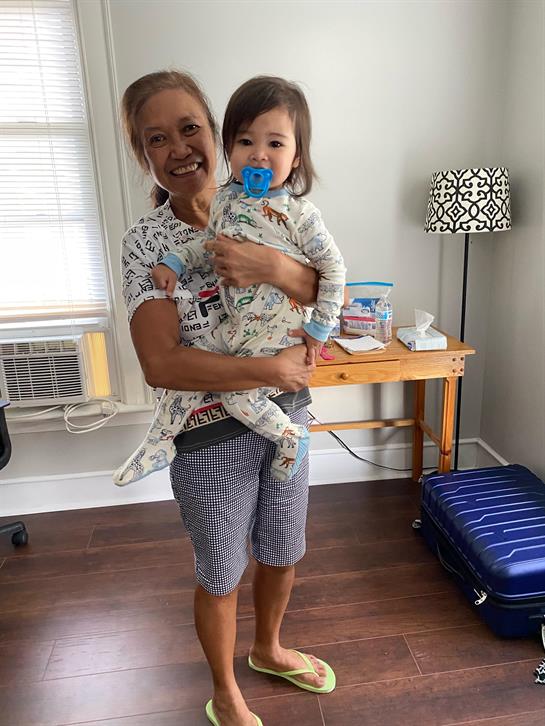 A woman smiles while carrying a child in a bright room with warm decor and personal touches.