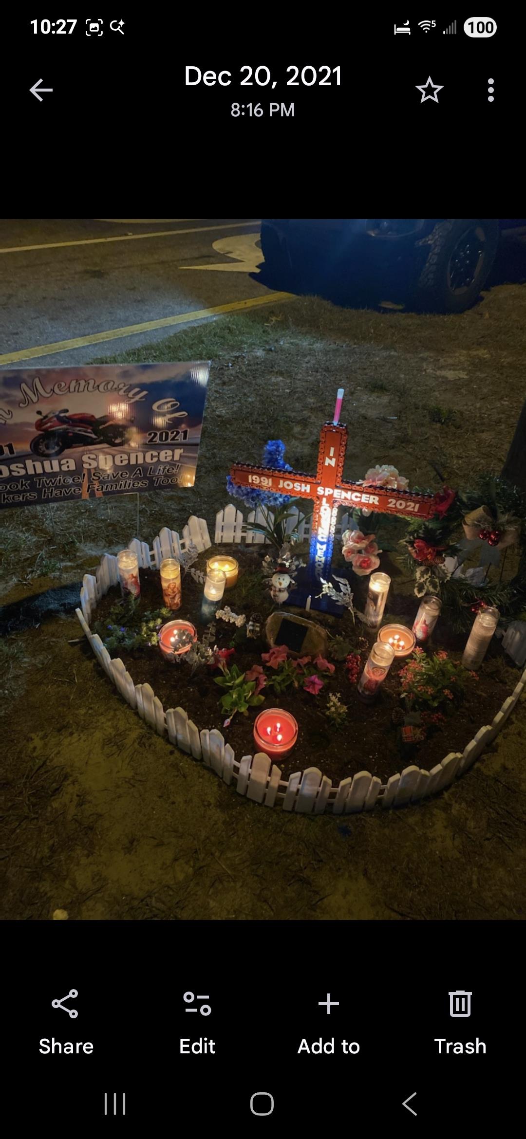 Vibrant tribute with candles, flowers, and a cross for Joshua Spencer in a public space.