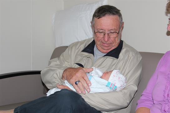 A caring grandfather cradles his newborn grandchild in a quiet hospital setting.