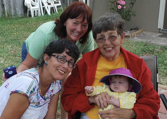Four generations come together in a warm backyard, enjoying each other's company and laughter.
