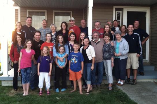 A cheerful group of family members enjoys a sunny day together outside a house, smiling and posing.