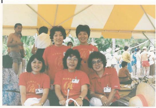 Five women in matching red shirts pose together in a joyful group under a large canopy.