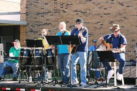 Musicians play various instruments on stage during a lively outdoor community event.