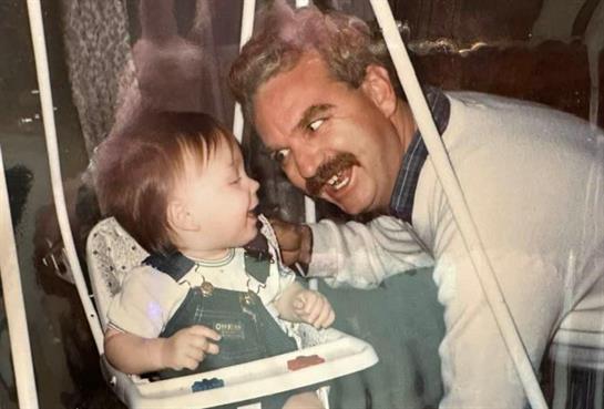 A father lovingly interacts with his baby in a swing while sharing smiles in a warm environment.