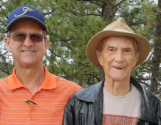 Two friends pose together outdoors, surrounded by trees, enjoying each other's company.