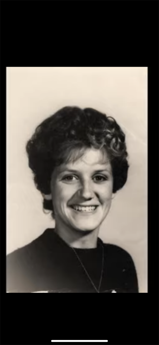 A young woman with curly hair smiles warmly while posing in a timeless black and white portrait.