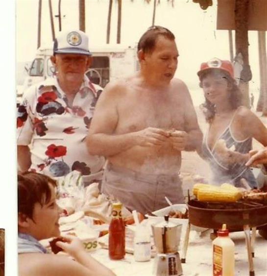 Group of people gathered around a grill at the beach, savoring food and enjoying the summer sun.