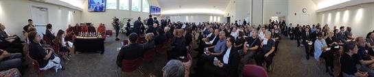 Hundreds of attendees are seated in a bright conference hall participating in discussions.