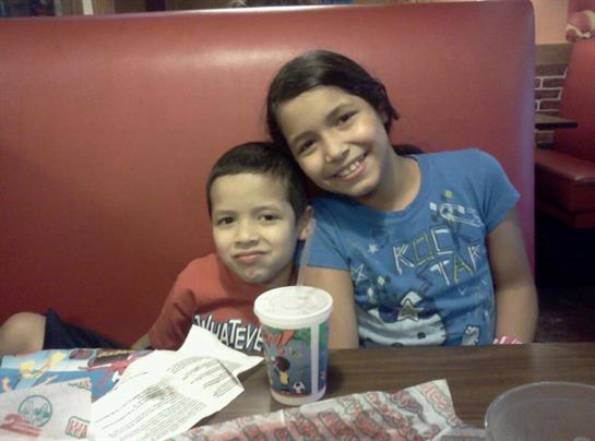 Two siblings sit side by side at a wooden table, enjoying their time together in a restaurant.