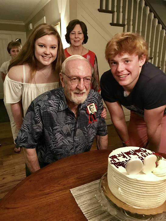 Family members gather around an elderly man to celebrate his birthday with a cake and joy.