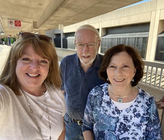Three people smile for a cheerful selfie on a sunny day in modern surroundings.