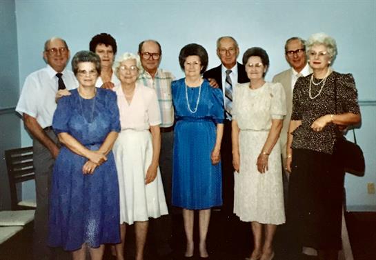 A group of older adults poses together, smiling and enjoying their time at a reunion.