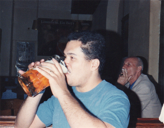 A man savoring a large mug of beer while seated in a bustling bar with others around.