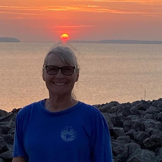 A joyful woman stands on rocky terrain, watching the sun setting over a tranquil lake.