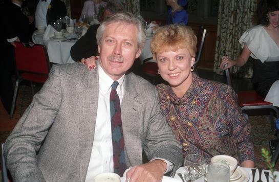 A couple seated at a table enjoying their time at a festive event with guests in the background.