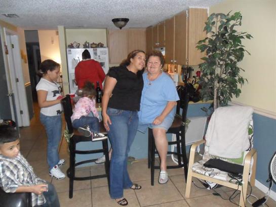 Two women pose happily while children are engaged in various activities at home.