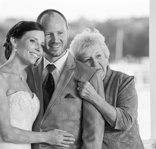 A happy couple poses for a portrait with an older woman during their wedding celebration.