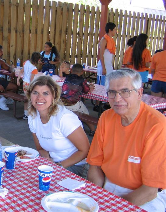 Friends and family sit at picnic tables, sharing food and laughter at a festive outdoor gathering.