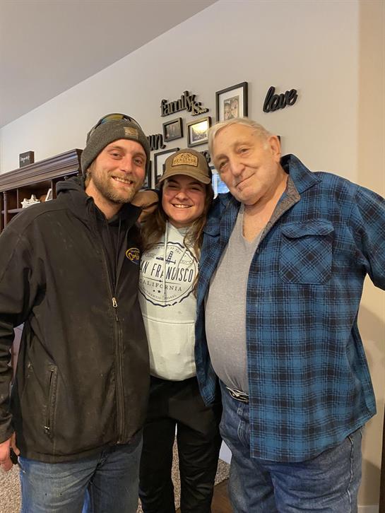 Three individuals share joyful moments during a family gathering in a warm indoor environment.
