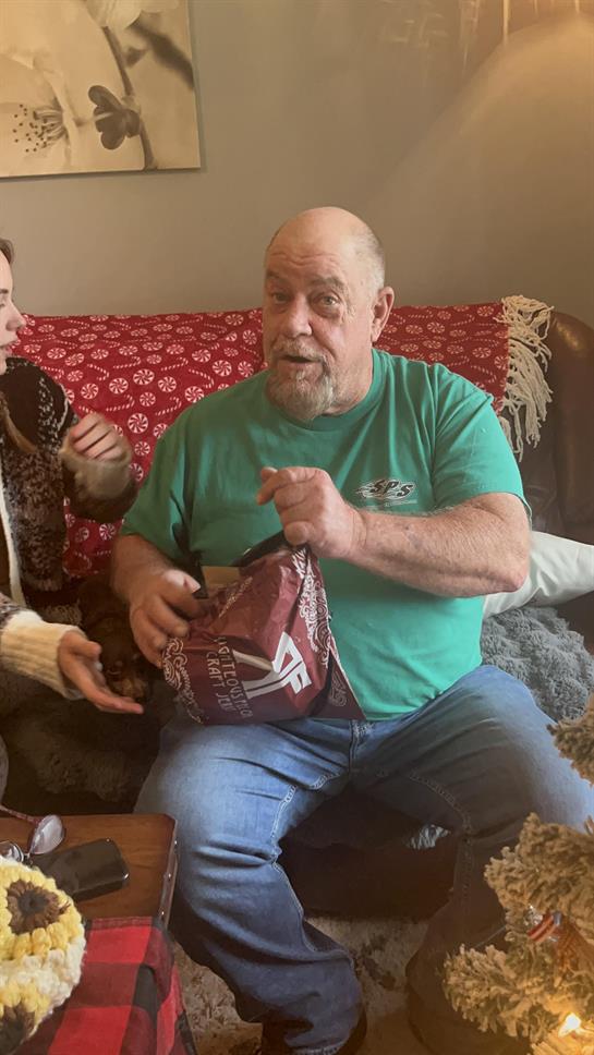 A man in a green shirt unboxes a gift as a woman excitedly watches.