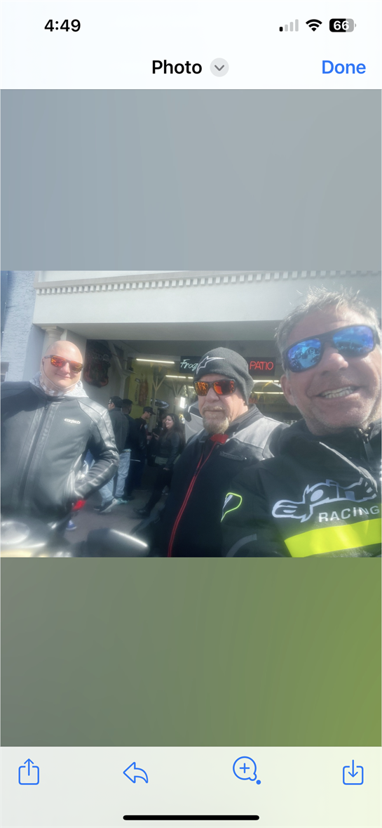 Three friends pose happily for a selfie during a motorcycle trip at a popular roadside stop.