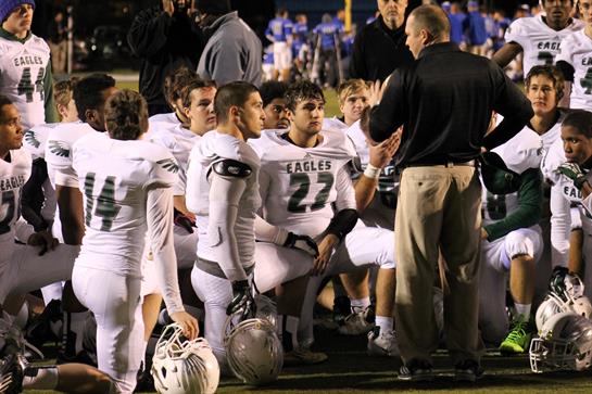 Players gather around their coach for strategy discussion during a night football game.
