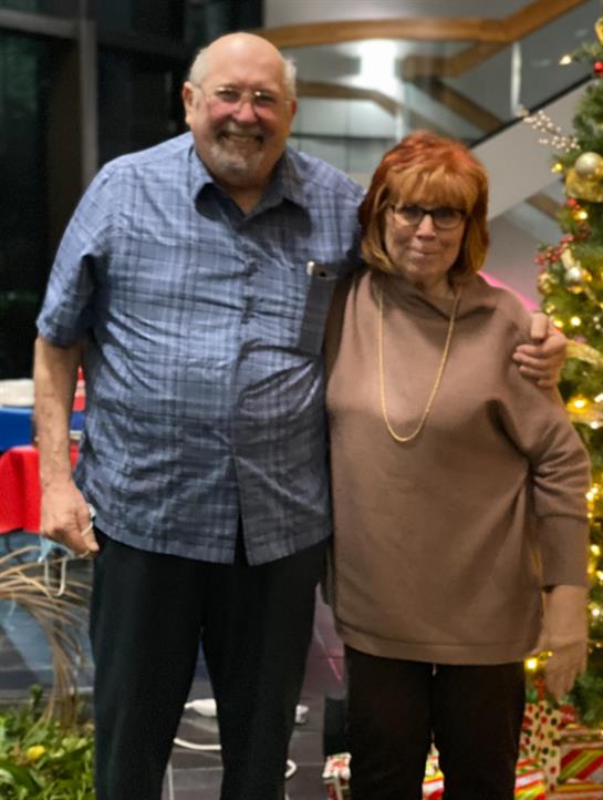 A cheerful couple stands side by side, smiling during a holiday celebration.