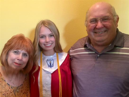 A young woman in a graduation gown smiles with her grandparents, celebrating her achievement.