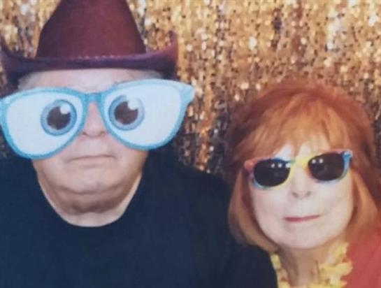 Two adults enjoy a lighthearted moment in large novelty glasses at a cheerful gathering.