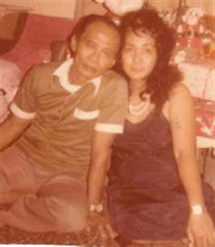 A couple sits closely together, smiling, in a vibrant living room filled with decorations.