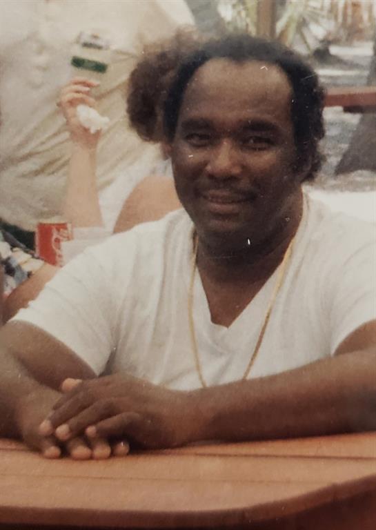 A cheerful man with a warm smile sits at a cafe table engaging with friends in a vibrant atmosphere.