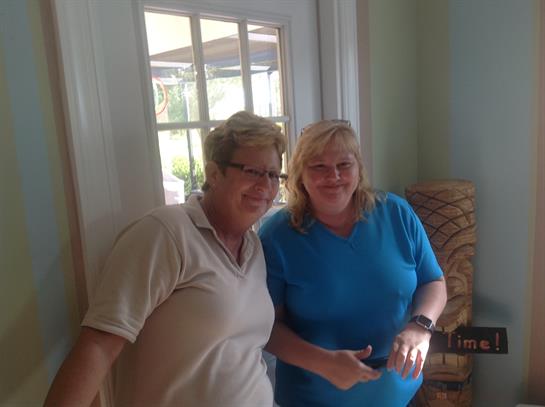 Two women are smiling and enjoying each other's company in a warm indoor space.