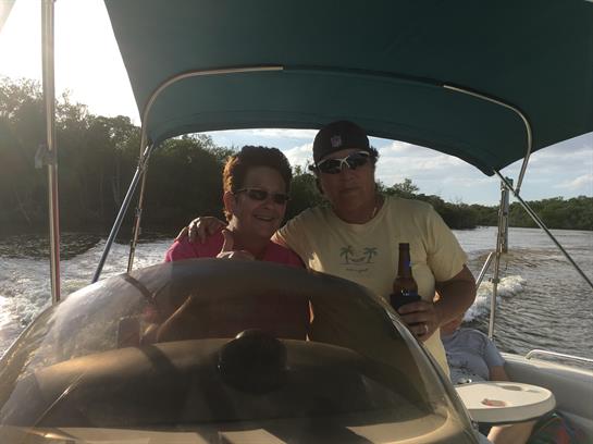 A couple navigates a boat while enjoying each other's company under a sunny sky.