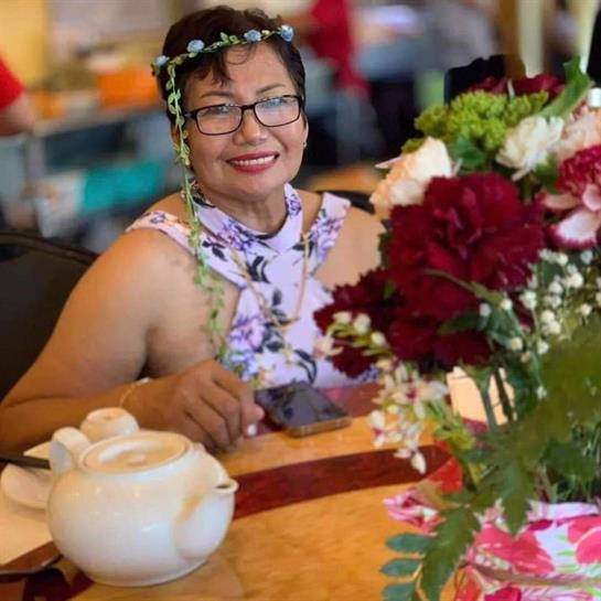 A smiling woman sits at a table adorned with vibrant flowers and a tea set, enjoying a social event.