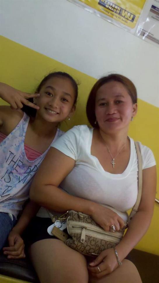 A cheerful girl poses with a peace sign next to a woman, both smiling happily in a colorful setting.