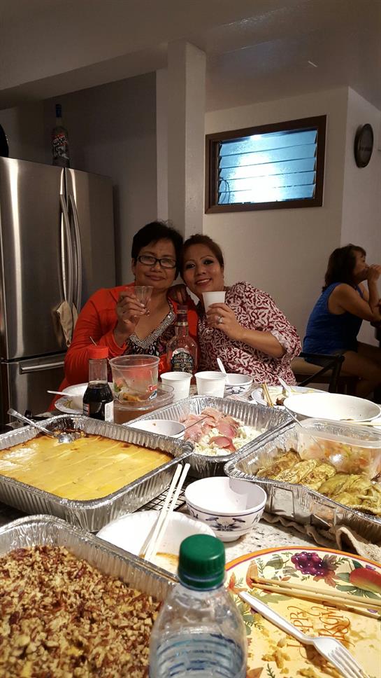 Two women celebrate together with drinks at a vibrant gathering surrounded by homemade food.