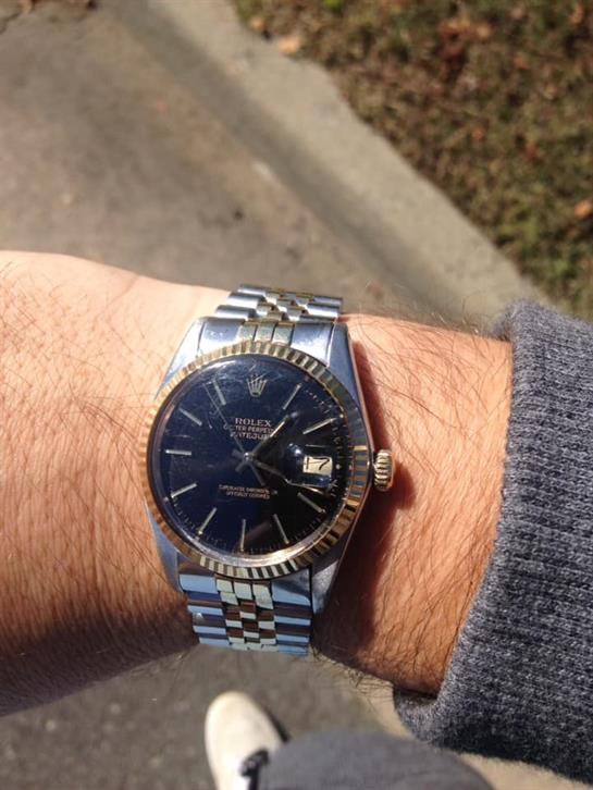 A silver watch with a dark face is worn on a wrist in bright sunlight, showcasing its features.