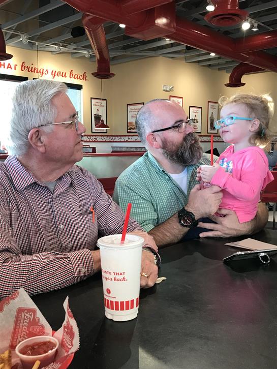 A grandfather, father, and young child share drinks and laughter in a vibrant restaurant.